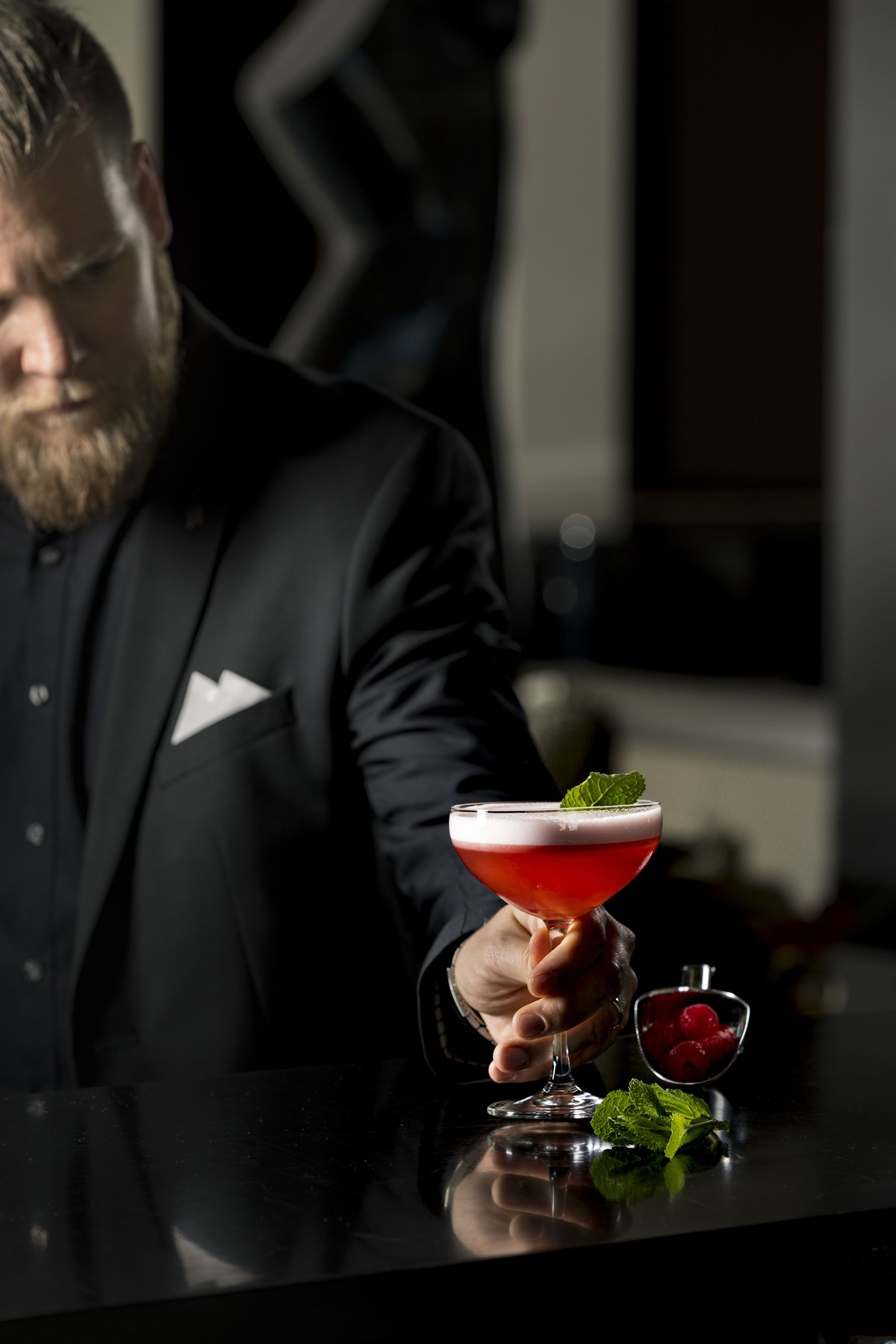 Barkeeper-Porträt mit Signature-Drink vor dunklem Hintergrund – Getränkefotografie mit Fokus auf Luxus und Licht.