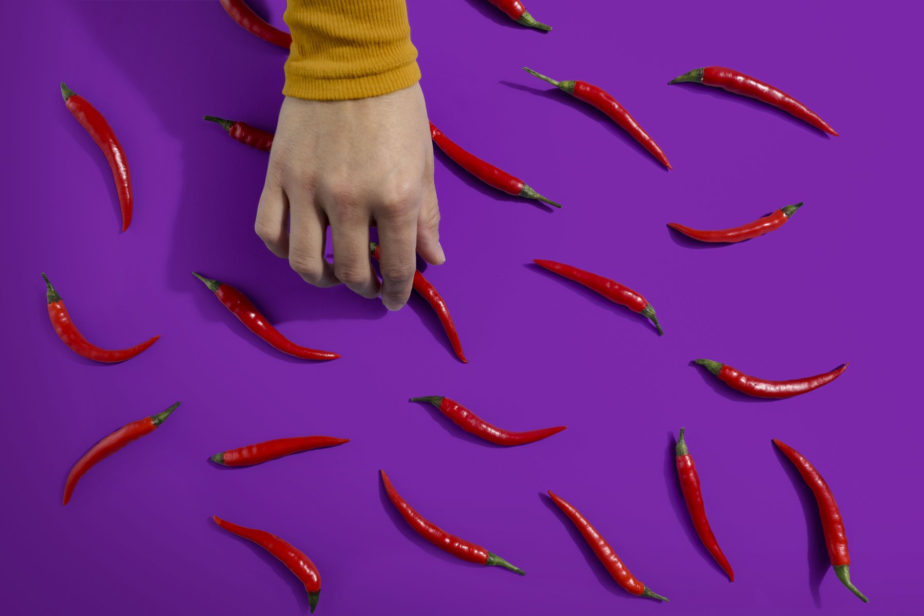 Hand interagiert mit einem Chili-Muster auf lila Grund – Werbefotografie