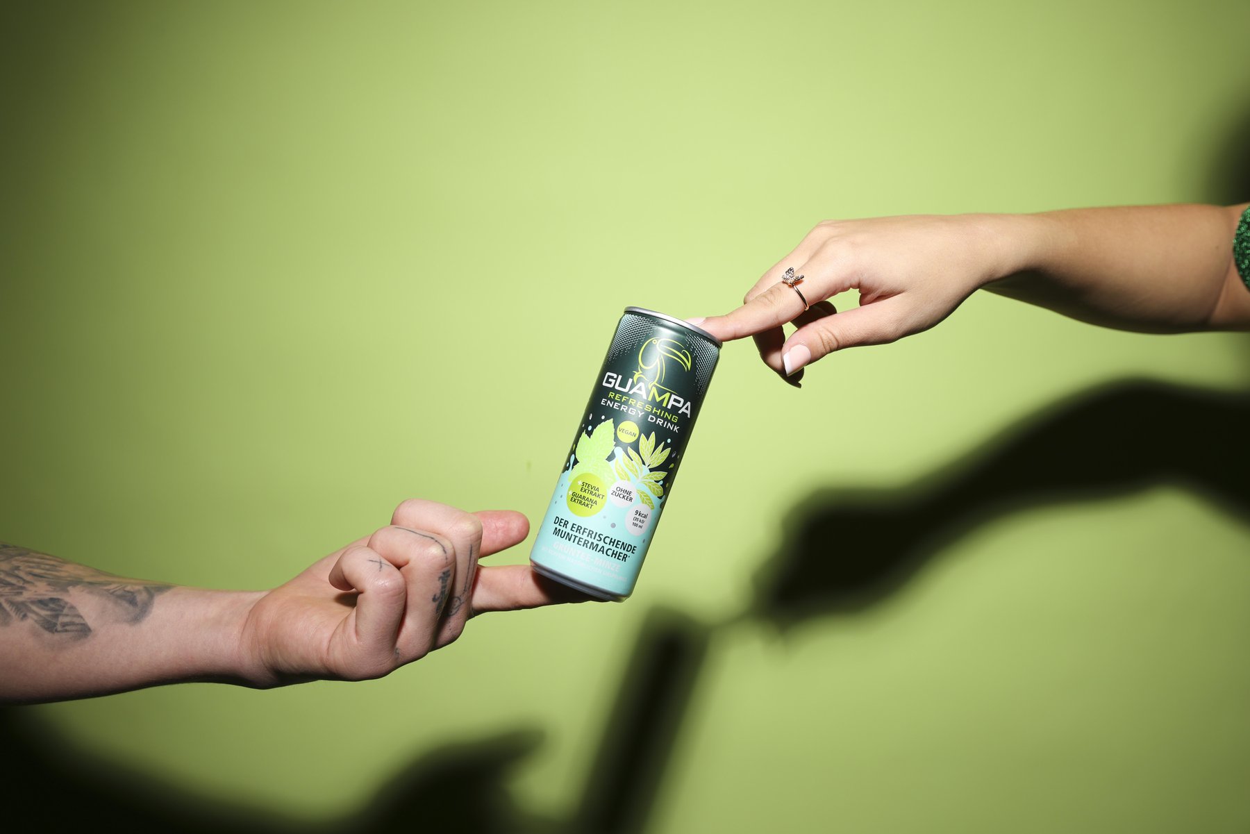 Zwei Hände balancieren eine Guampa Energy Dose vor grünem Hintergrund