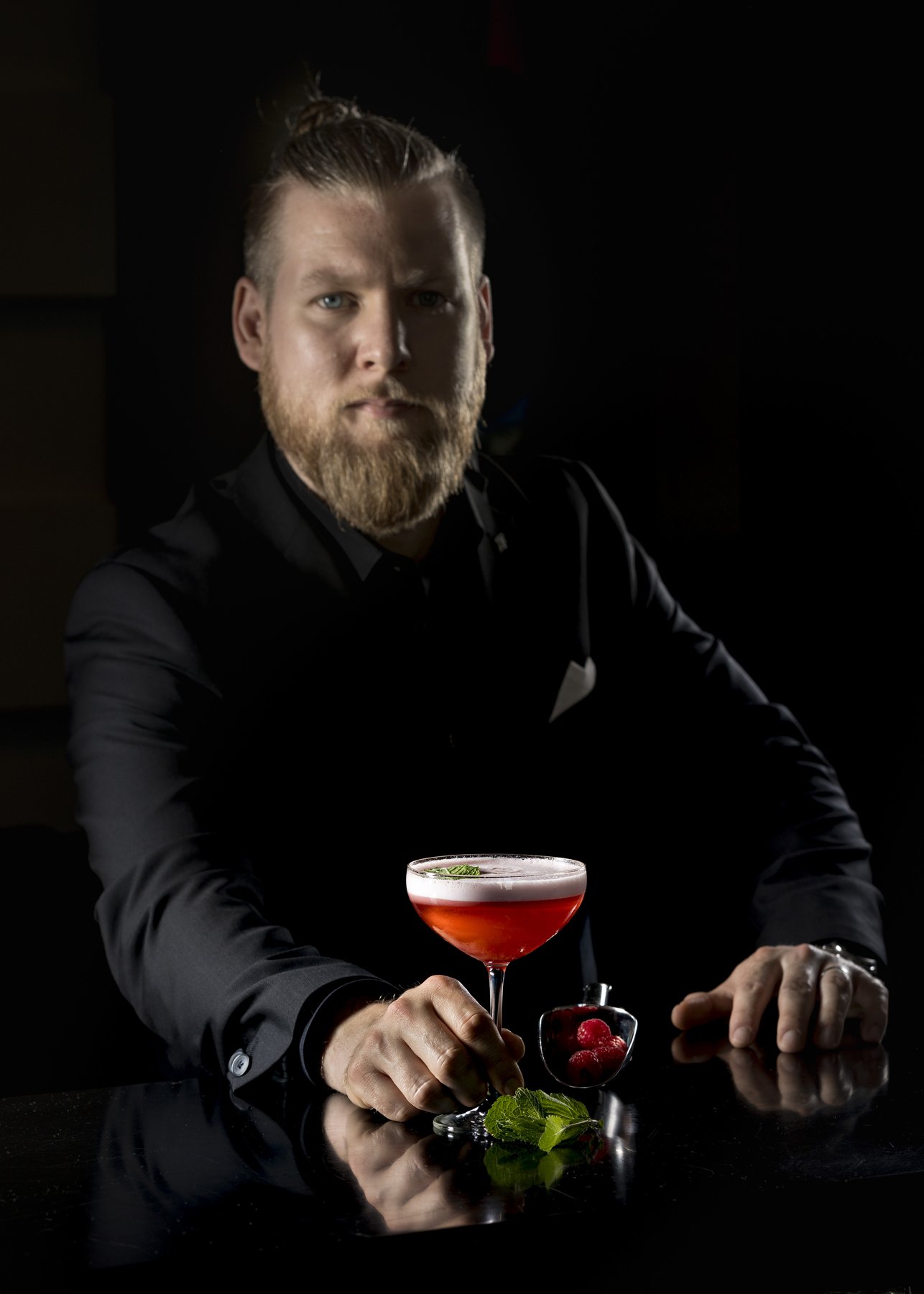 Dark-Moody-Porträtfotografie: Barkeeper mit kunstvollem Drink – Fokus auf Lichtsetzung und Exklusivität.