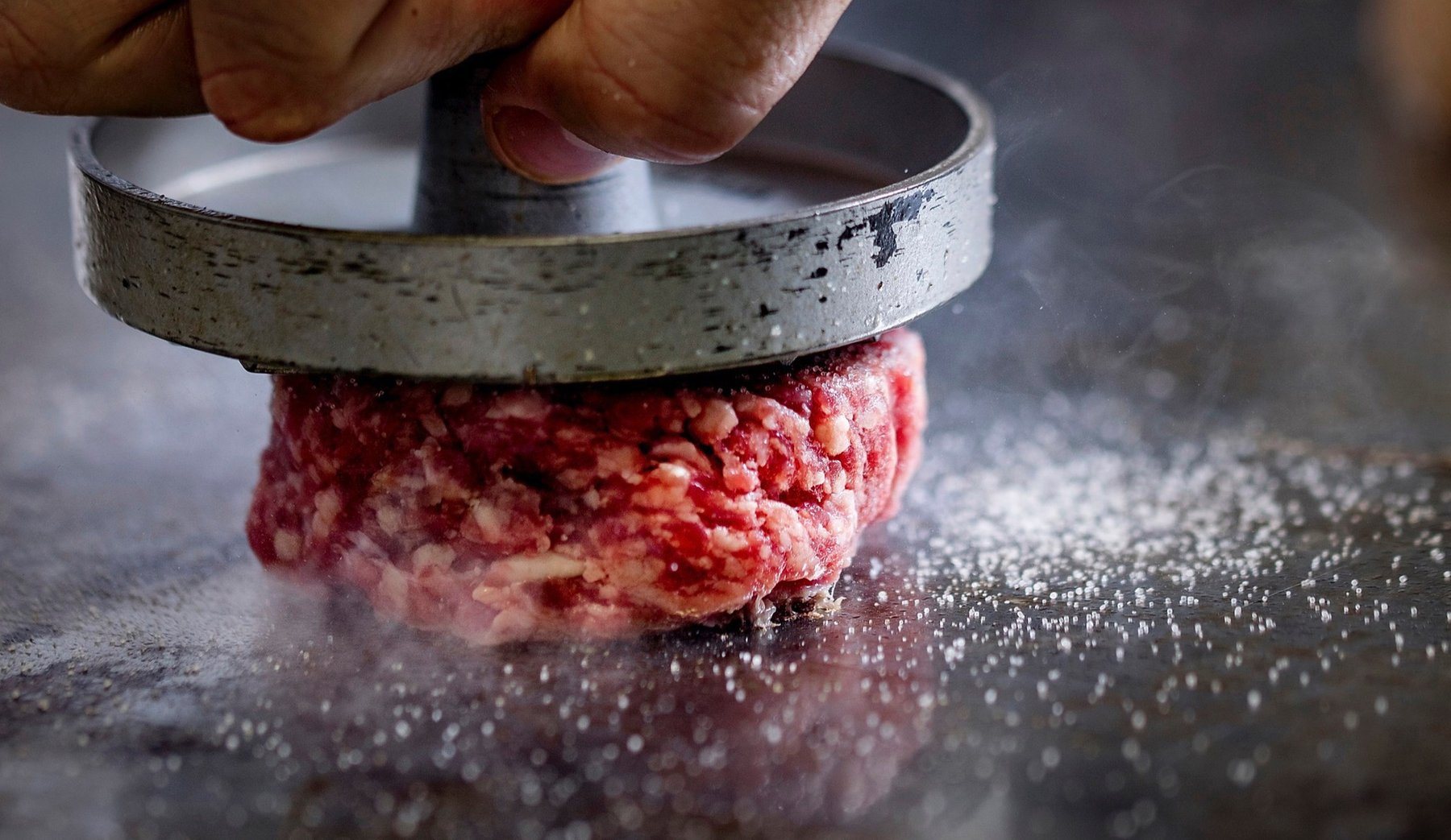 Detail beim Grillen und Smashen frischer Burger-Patties
