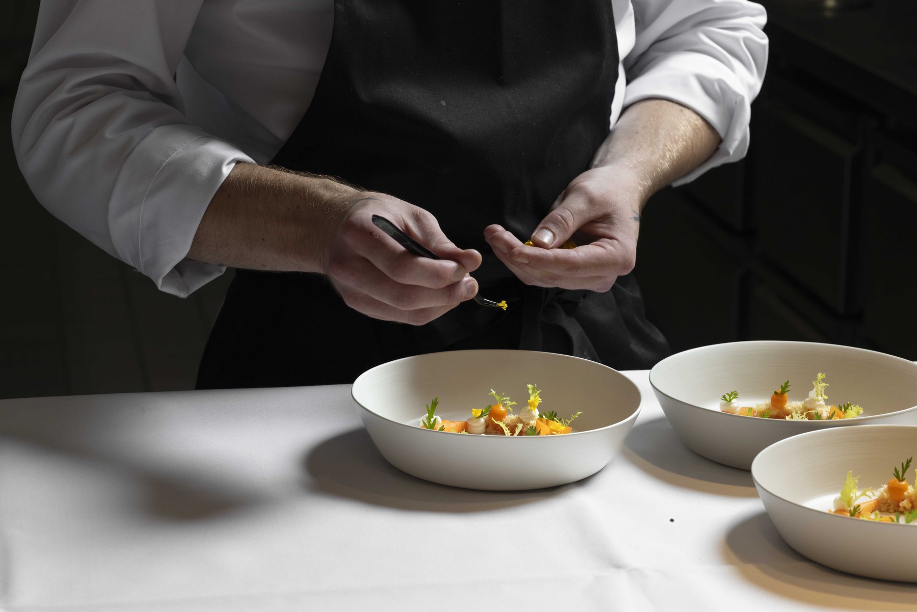Koch beim Anrichten eines Fine-Dining-Gerichts – High-End Foodfotografie, Fokus auf Kulinarik und Handwerk von Kitchenkiss.