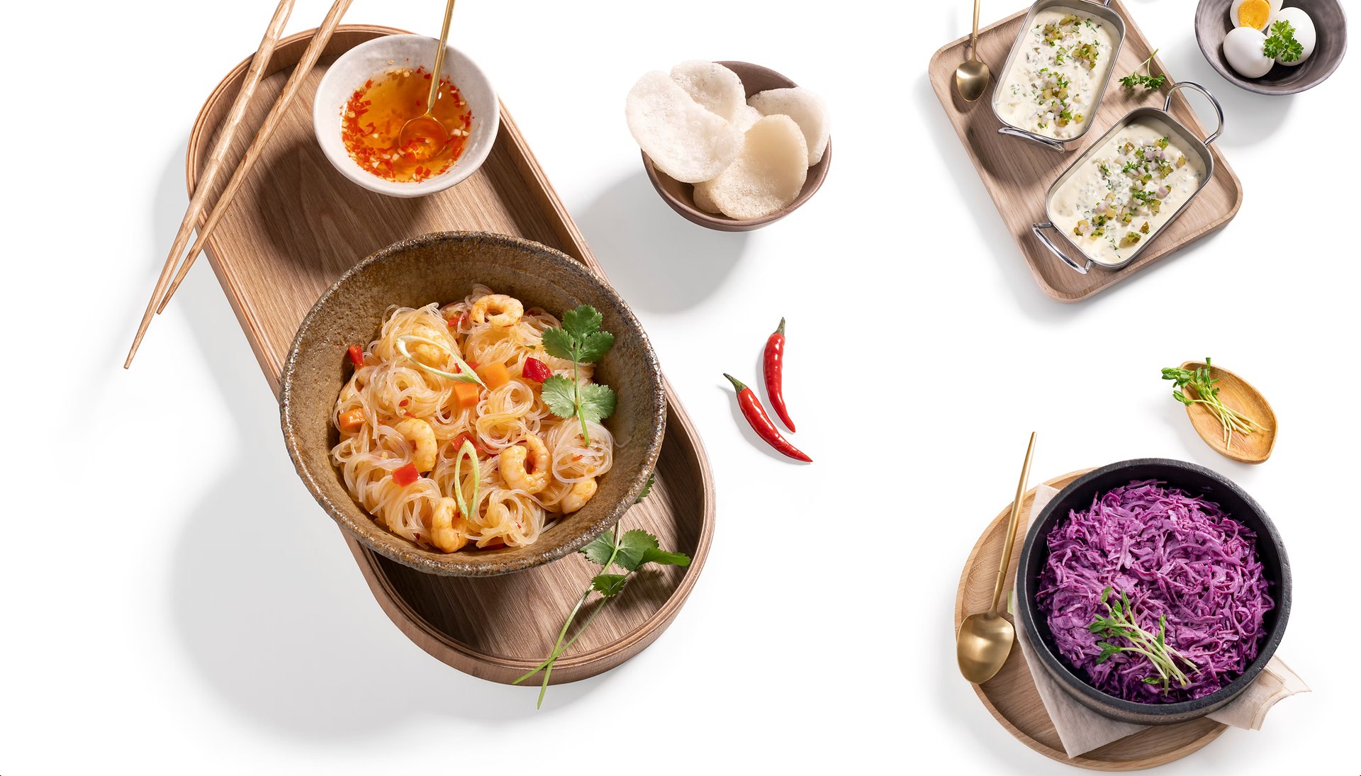 Aufsicht auf Glasnudelsalat mit Garnelen, Rotkohlsalat und Dips auf Holztabletts – Feinkost-Fotografie auf Weiß für Kugler