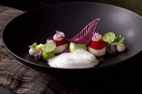 Fine-Dining-Gericht mit essbaren Blüten und Schaum in schwarzer Keramikschale
