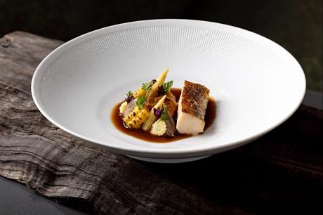Fischgericht mit Jus in weißer Schale auf Altholz
