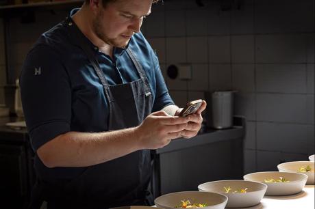 Koch fotografiert sein Gericht mit dem Smartphone in der Küche