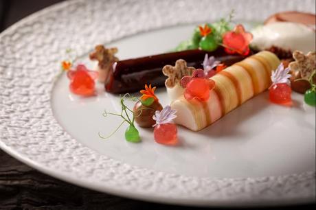 Dessert mit Sorbet-Röllchen und essbaren Blüten auf strukturiertem Teller